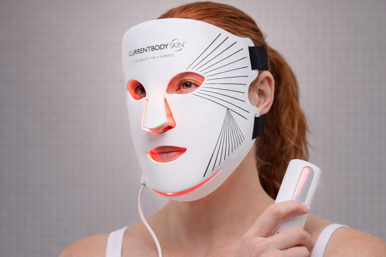 Red-haired woman wearing the CurrentBody Skin LED light therapy mask during an at-home skincare treatment